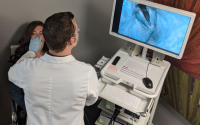 Clinician in a white coat and mask performing an endoscopy on a patient, with a monitor showing the internal view.