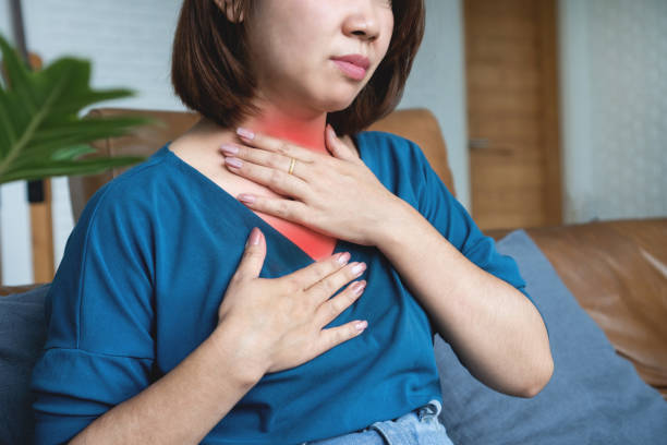 Woman seated on a couch touches her throat with a red highlight around the neck indicating throat pain or choking discomfort.