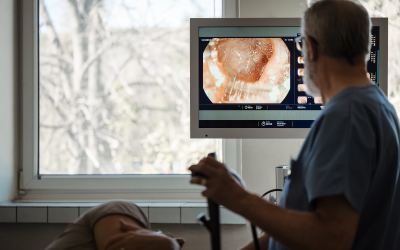 Healthcare professional performing an endoscopic examination on a patient; monitor shows live internal tissue view.