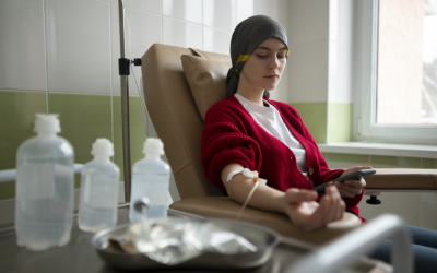 Woman donating blood sits in a recliner wearing a red sweater, with a needle in her arm and looking at a phone.