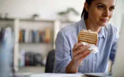 Diet and urban lifestyle | dr. Vipulroy rathod | dr. Vipulroy rathod Woman at a desk in an office holds a slice of layered cake with cream, looking toward the camera.
