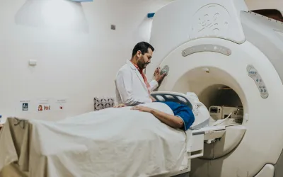Imaging | dr. Vipulroy rathod | dr. Vipulroy rathod Medical technician beside a patient on an examination table, preparing to insert them into a large MRI scanner in a clinical room.